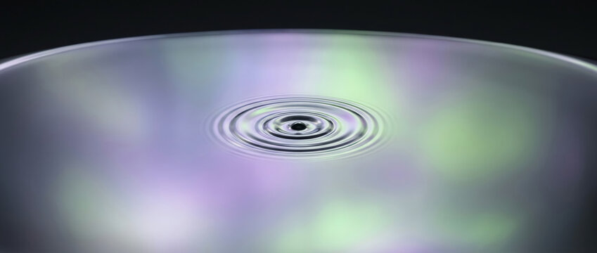 Macro water ripple on iridescent liquid surface with purple and green reflections, serene ethereal mood, minimalist abstract high-speed photography background.