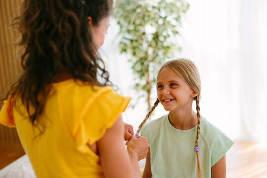Mother braiding her daughter's hair while the girl smiles during a family morning routine