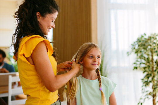 Mother gently braiding her young daughter's hair at home while preparing her for the day