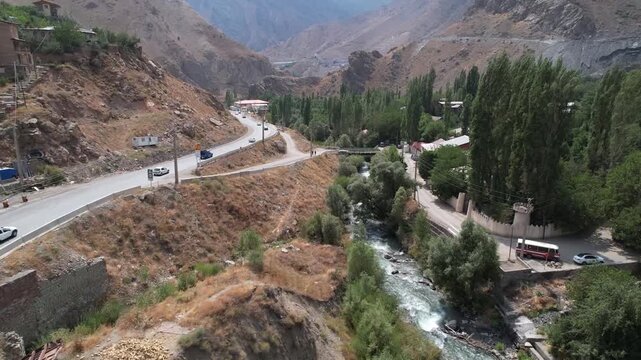 Chalus Road highway runs beside a river and poplar line through a dry mountain slope, showing traffic corridor and valley water. Ideal for travel, tourism, and nature stock Iran Alborz.