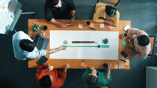 A diverse group of professionals collaborates in a modern office, focusing on strategies for achieving carbon neutrality by 2050, highlighting teamwork and innovation. Raster