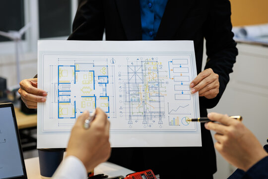 Business team reviews a printed technical floor plan and system diagram in a modern office, pointing at details during a project meeting.