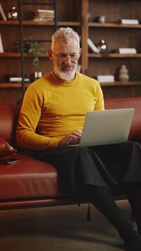 Stylish silver-haired male freelancer types on laptop while working from home