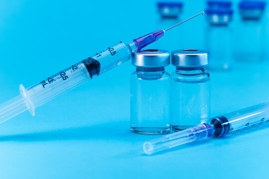 medical syringe with needle next to vaccine medicine glass vials on blue background as a conceptual backdrop for pharmaceutical research healthcare immunization biotechnology and clinical science