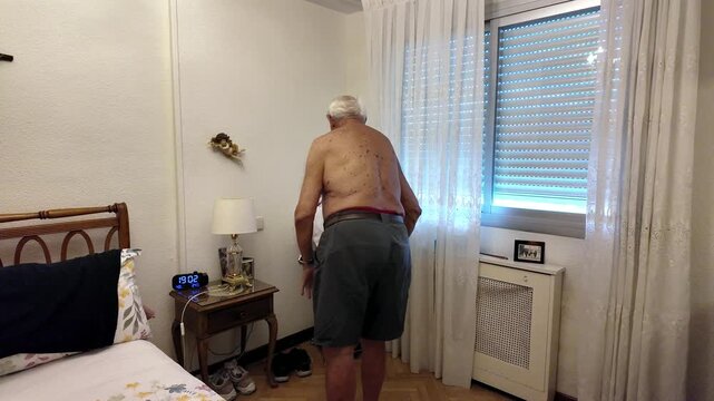 Elderly man putting on a t shirt in his bedroom