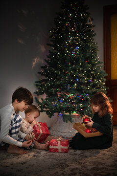  family of three children are celebrating New Year's and Christmas under the Christmas tree at home, opening presents. A quiet, cozy family evening. vertical