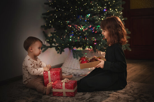 Two little girls, an older and younger sister, decorate the New Year's tree with baubles. Children are getting ready for Christmas. Christmas Eve. A magical, festive, fairytale night.