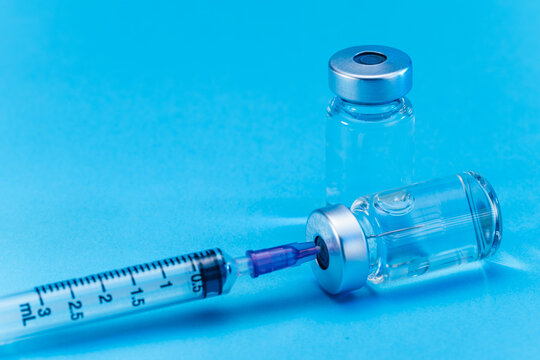 medical syringe with needle next to vaccine medicine glass vials on blue background as a conceptual backdrop for pharmaceutical research healthcare immunization biotechnology and clinical science