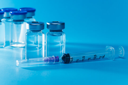 medical syringe with needle next to vaccine medicine glass vials on blue background as a conceptual backdrop for pharmaceutical research healthcare immunization biotechnology and clinical science