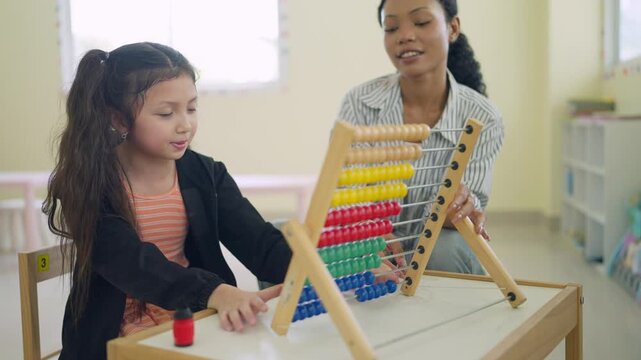 Young girl concentrates on colorful abacus with teacher beside her. Teacher smiles gently, guiding her through math learning