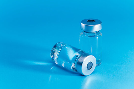 medical syringe with needle next to vaccine medicine glass vials on blue background as a conceptual backdrop for pharmaceutical research healthcare immunization biotechnology and clinical science