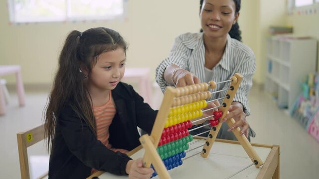 Young girl concentrates on colorful abacus with teacher beside her. Teacher smiles gently, guiding her through math learning