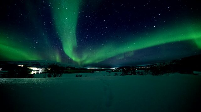 Time lapse of green Aurora Borealis dancing over snow-covered ground in Skogsfjord, Norway