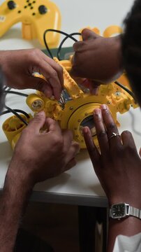 Vertical shot of multiethnic young adults assembling yellow robot prototype. Footage is perfect for promoting STEM education, robotics engineering courses and technology workshops