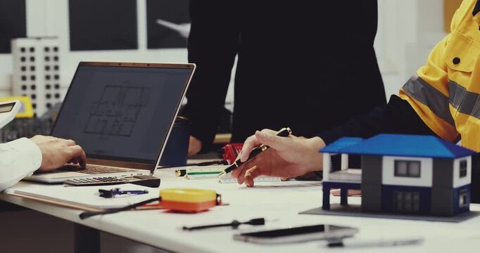 Architects review house plans at a desk with a laptop, measuring tools, color samples and a modern scale model for a home design project.