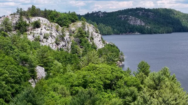 Drone view across a forested rocky bluff beside a calm wilderness lake in Whitefish Falls Ontario Canada