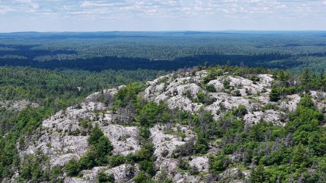 Drone circles a rounded granite crown broken by deep cracks and scattered conifers above an endless northern forest