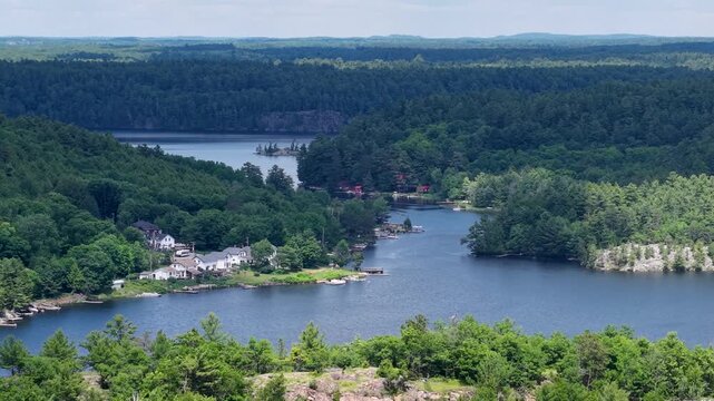 High drone view overlooks homes clustered around winding forest lake coves and rocky shorelines in the Whitefish Falls community