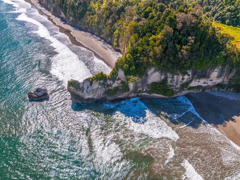 Aerial view of the rugged coastal cliffs and sandy beach in Kaur Regency, Bengkulu, Indonesia.
