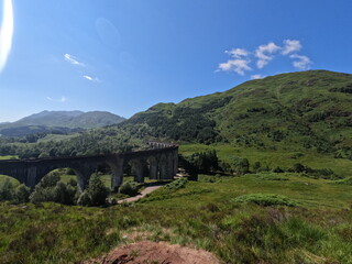 Naklejka premium Historic Glenfinnan Viaduct curved concrete railway bridge in lush green mountains of Scottish Highlands, iconic Scotland landmark.