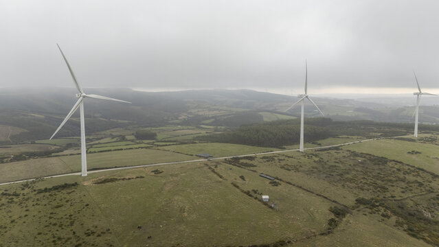 Aerial view of Parque eolico Neda with wind turbines on a grassy hillside under a cloudy sky in Lugo, Lugo, Spain.
