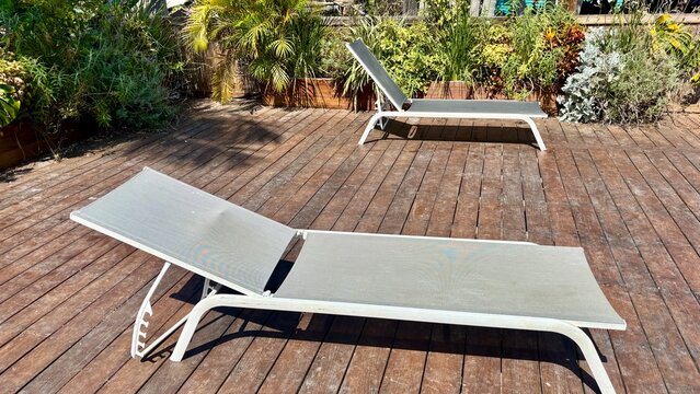 White poolside lounge chairs on a wooden deck surrounded by lush greenery, creating a relaxed outdoor leisure setting
