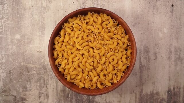 Rotation of macaroni in wooden bowl on a concrete table. Top view	
