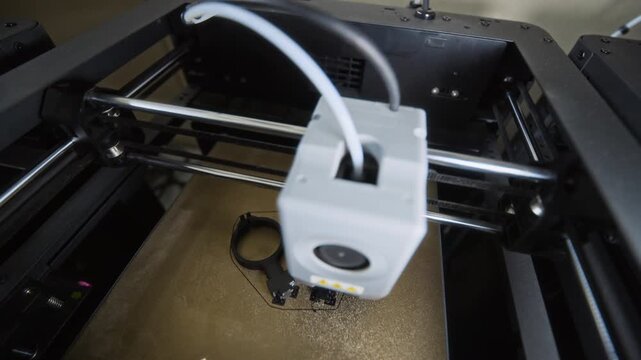 3D printer printing black plastic robotic components in close up high angle shot. Footage is suitable for promotional videos on additive manufacturing and engineering technology