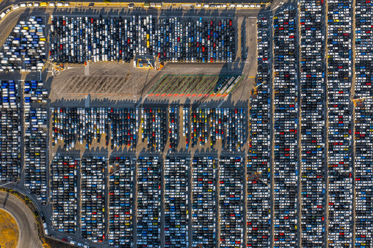 Aerial view of a vast automotive storage lot filled with rows of new cars parked in an organized grid pattern in Civitavecchia, Lazio, Italy.