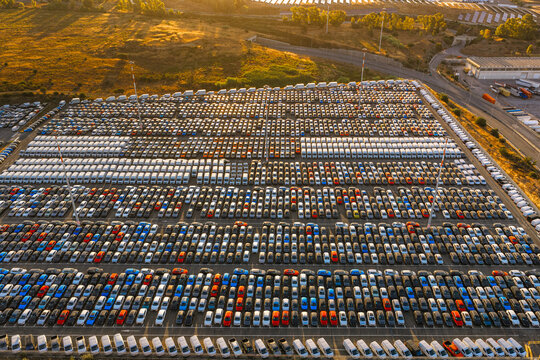 Aerial view of a vast automotive storage lot filled with rows of new cars under the warm glow of the golden hour in Civitavecchia, Lazio, Italy.
