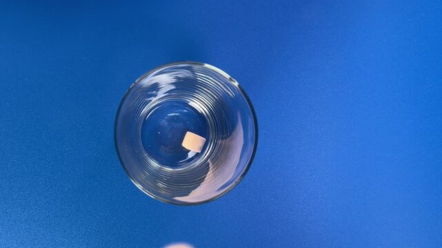 Colorful marshmallow pieces falling into glass bowl on blue background, with multiple pieces dropping through the air during playful food action and dynamic movement