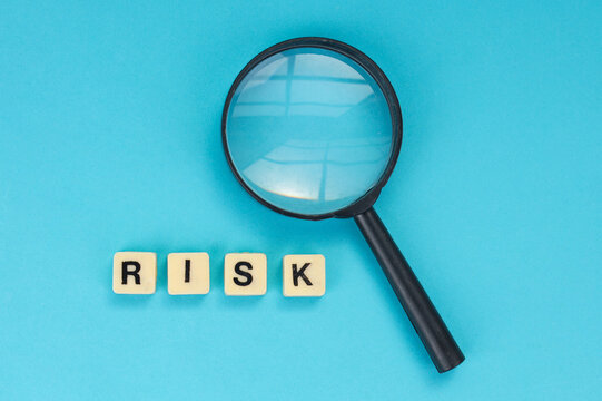 Top View of Risk Block Letters with Magnifying Glass on Blue Background