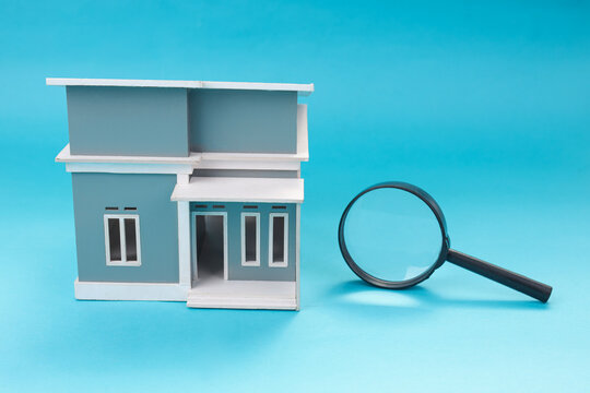 Closeup of Miniature Home Beside Magnifying Glass Isolated on Blue Background