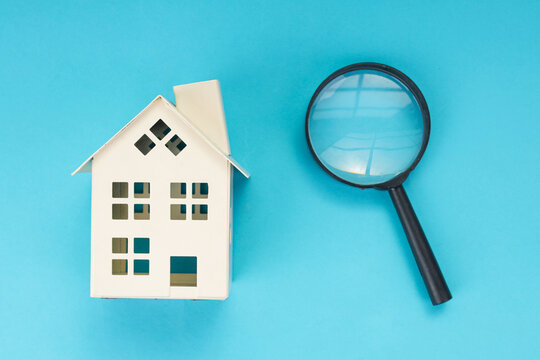 Top View of Miniature House with Magnifying Glass on Blue Background