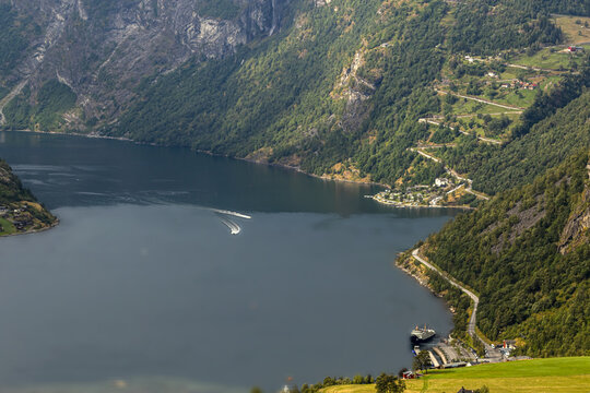 Aerial view of Geirangerfjord featuring steep mountains, lush green slopes, winding roads, and boats on the deep blue water in Stranda Municipality, More og Romsdal, Norway.