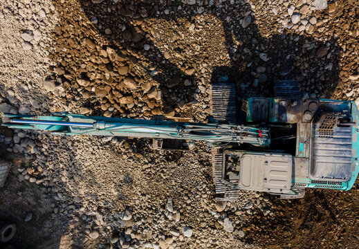Aerial view of an excavator parked on a rocky riverbed with gravel and stones in Karanglewas, Central Java, Indonesia.