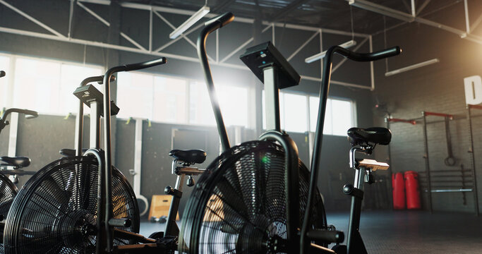 Empty, fitness and air bike in gym for cardio, wellness facility and setup for spin class with gear. Stationary bicycle, interior and equipment in training studio for cycling, development or machine