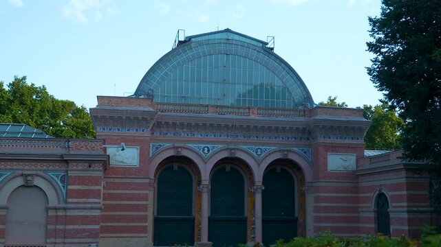 A wide shot of the Palacio de Velazquez facade featuring its iconic glass dome and brick architecture in Madrids Retiro Park. Suitable for travel and history documentaries.