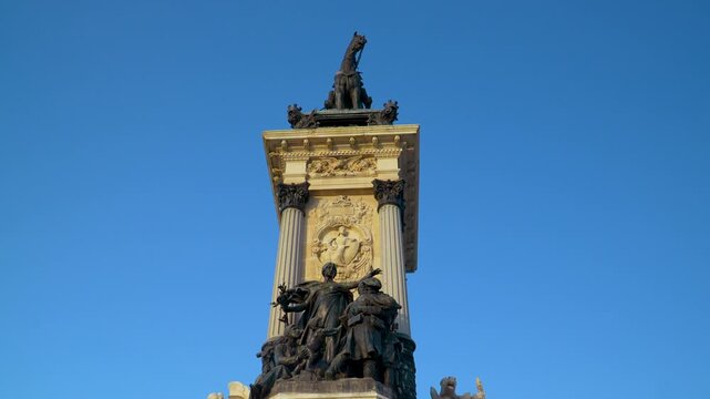 A low angle shot of the ornate stone and bronze sculptures on the Monument to Alfonso XII in Madrid. Suitable for travel documentaries and European history content.