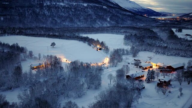 Snowmobiles with headlights on navigate snowy Norwegian landscape, aerial