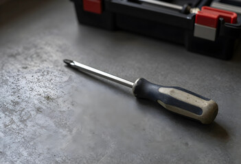 Fototapeta premium Home improvement and diy repair concept, screwdriver tool on a concrete surface with a toolbox in the background