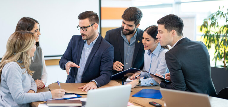 Manager explains ideas and guides a collaborative planning session while colleagues listen and take notes in a modern office.