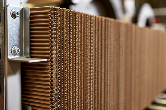 A close up view of layered corrugated cardboard sheets held in an industrial machine. This detailed texture shot highlights sustainable packaging material manufacturing.