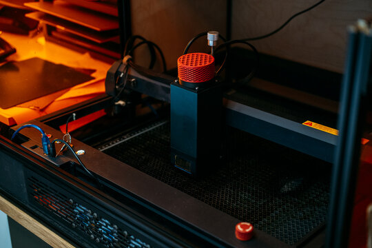 Diode laser module with red cover stands on honeycomb bed of desktop engraving machine. laser engraver, desktop diode laser machine, 30w laser module