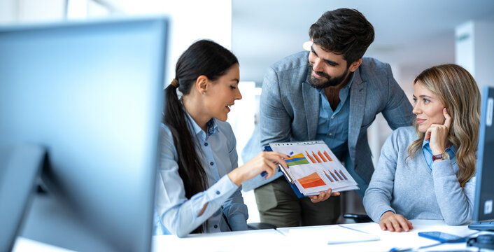 Business colleagues analyzing financial charts and discussing data reports on clipboard in office