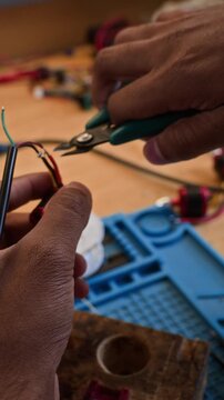 Vertical video of technician taking wire cutters from pegboard and cutting electrical wires on robotic component. Video is perfect for engineering and robotics promos