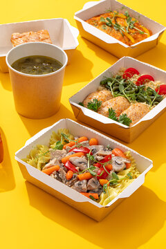 Nutritious balanced daily meal prep ration with farfalle pasta chicken cutlets soup and omelet in craft containers on yellow background