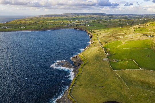 Aerial view of the Cliffs of Moher featuring lush green fields, traditional stone walls, and the rugged coastline meeting the Atlantic Ocean in County Clare, Ireland.