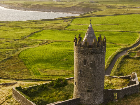 Aerial view of Doonagore Castle surrounded by lush green fields, stone walls, and the Atlantic coastline in Doolin, County Clare, Ireland.
