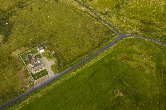 Aerial view of a rural house with a walled garden surrounded by lush green fields and a winding road in Doolin, County Clare, Ireland.